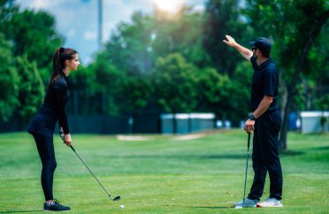 Playing golf. Young woman playing golf with golf instructor